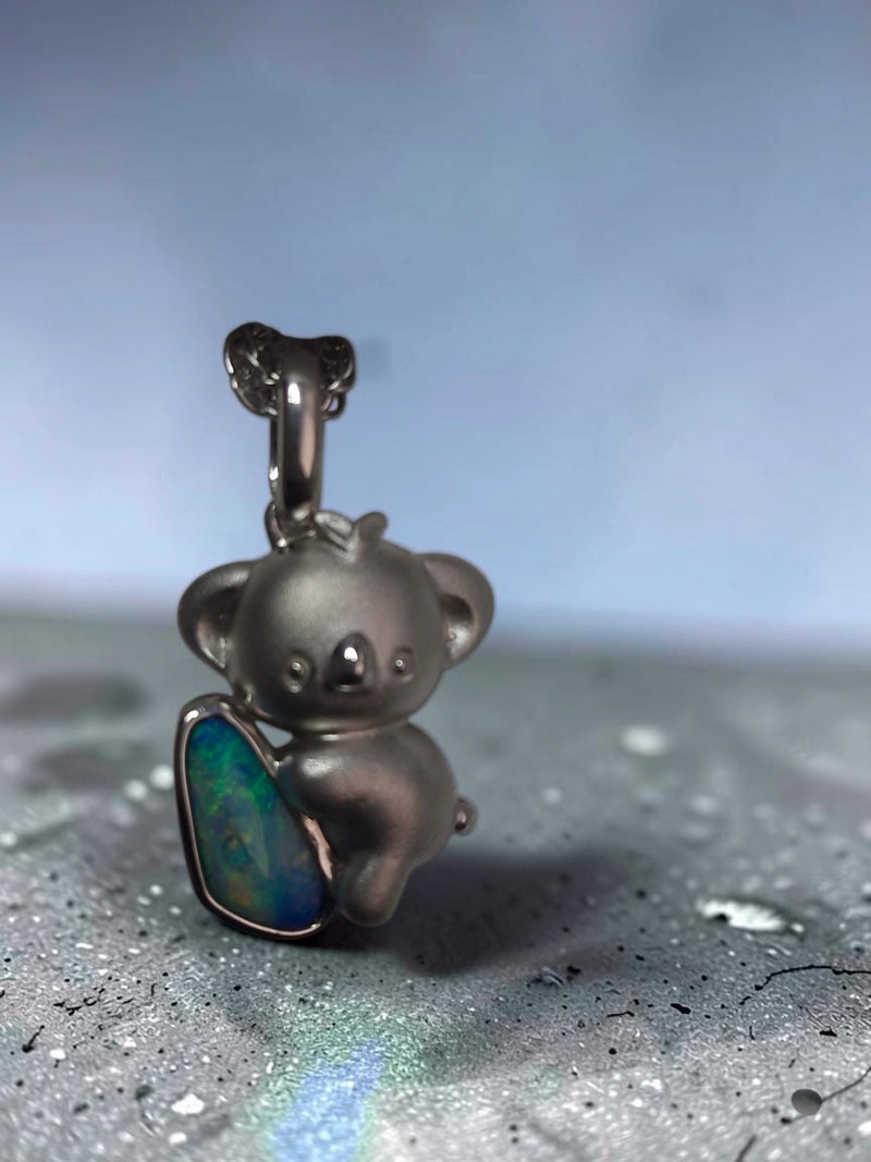 Time & Lustre sterling silver koala pendant featuring a vibrant Australian opal inlay on a textured grey surface.
