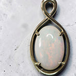 Time & Lustre oval opal pendant featuring a cabochon gemstone in a polished gold infinity-style four-prong setting.