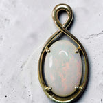 Time & Lustre oval opal pendant in a polished gold infinity-style frame with a cabochon-cut gemstone.