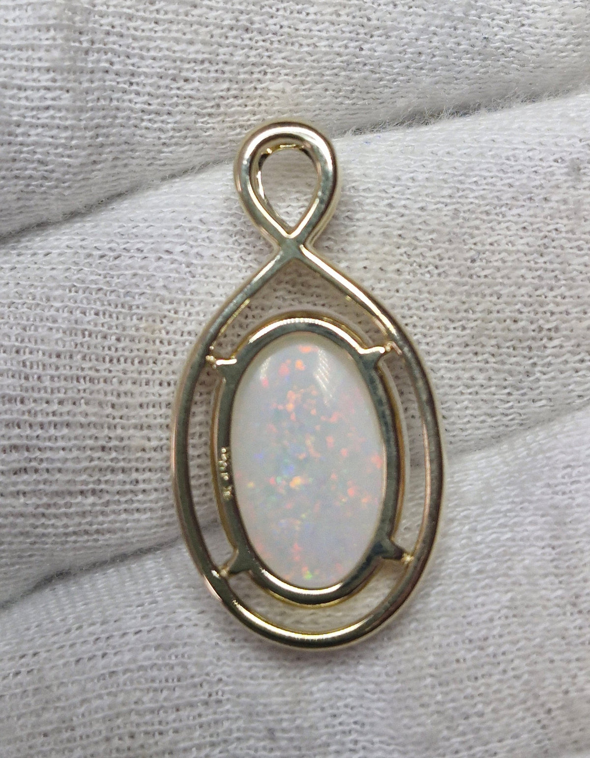 Time & Lustre oval opal pendant featuring a cabochon gemstone with vibrant flashes in a polished gold infinity bail.