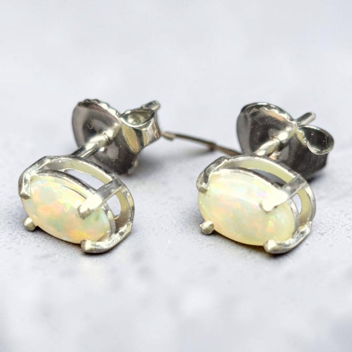 Time & Lustre oval opal stud earrings featuring iridescent cabochon stones in a classic four-prong metal setting.