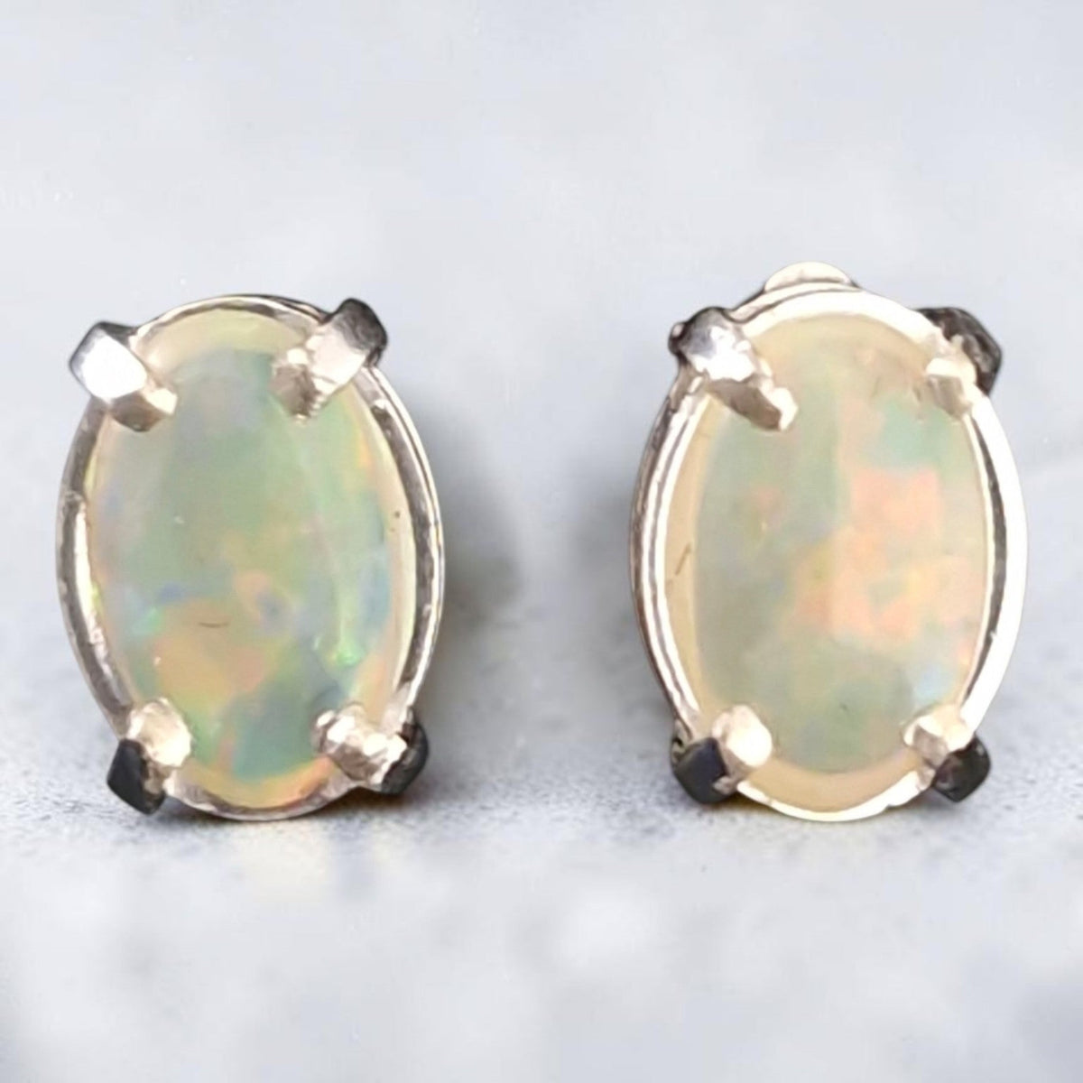 Time & Lustre oval opal stud earrings featuring iridescent cabochon stones in a classic four-prong metal setting.