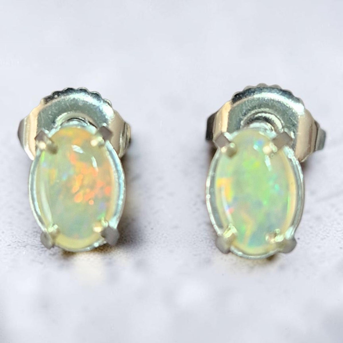 Time & Lustre oval opal stud earrings featuring iridescent cabochon stones in a classic four-prong metal setting.