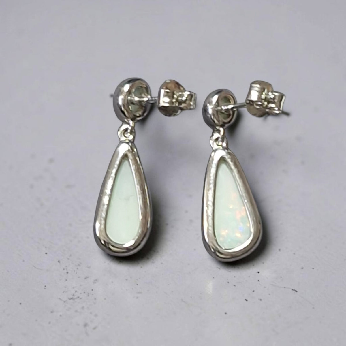 Time & Lustre teardrop opal drop earrings in polished sterling silver with post-back closures on a grey surface.