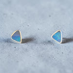 Time & Lustre triangle stud earrings featuring blue and teal opals set in minimalist sterling silver on grey stone.